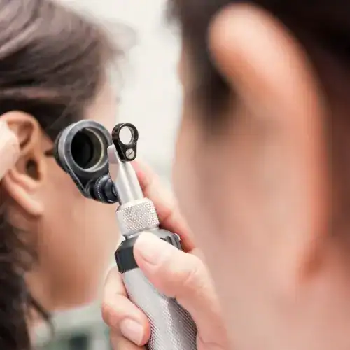 Audiologist examining patient’s ear canal with otoscope during hearing evaluation