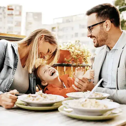 Parents laughing with child while sharing a meal together at outdoor restaurant
